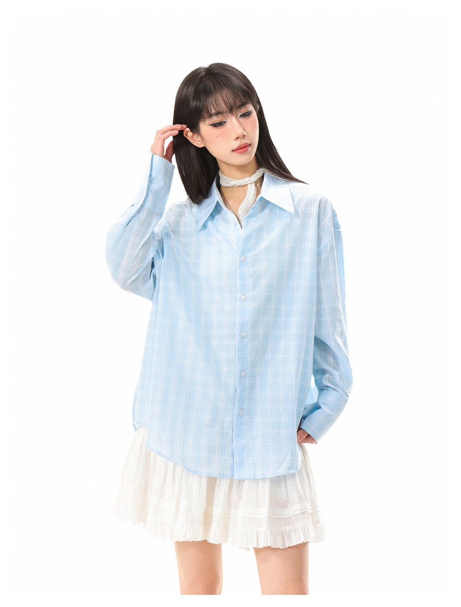 Model wearing a light-blue plaid button-up shirt over a white ruffled skirt, shown from the front.