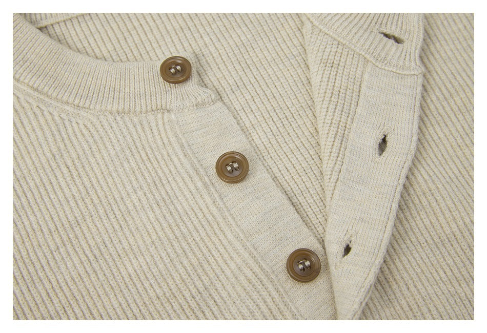 Close-up of a cream rib-knit neckline and placket with three brown buttons.
