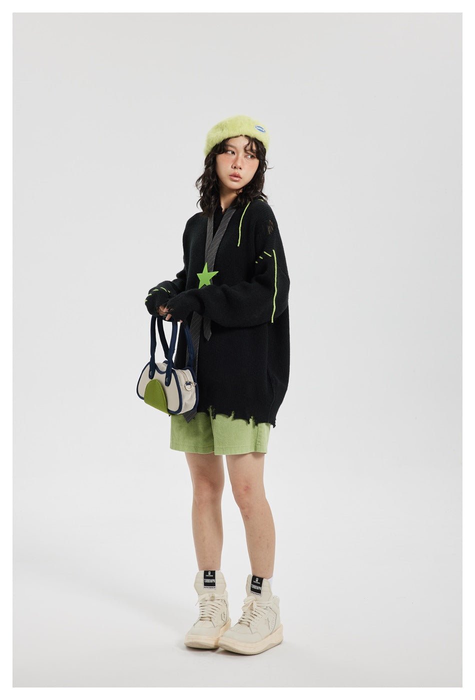 Model wearing an oversized black distressed knit sweater with green stitching, green shorts and cream sneakers
