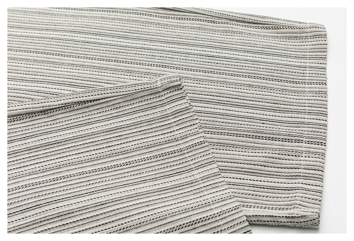Close-up of cream fabric with thin black and gray stripes, folded to show its texture and edge.
