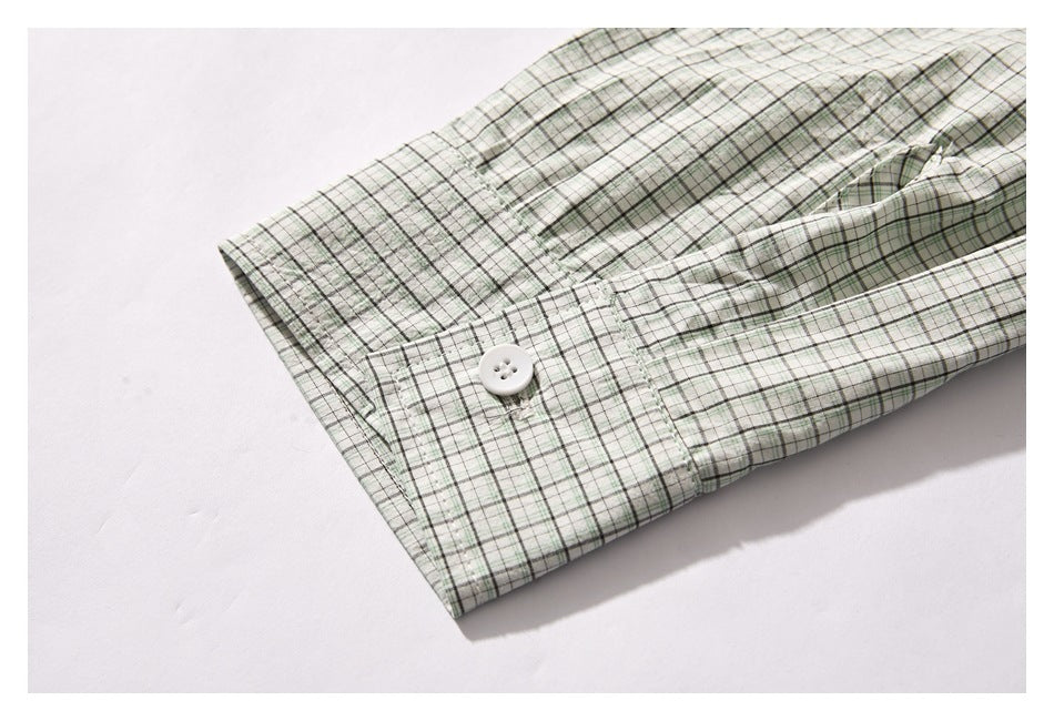 Close-up of a white buttoned cuff on a pale green and white plaid shirt sleeve.