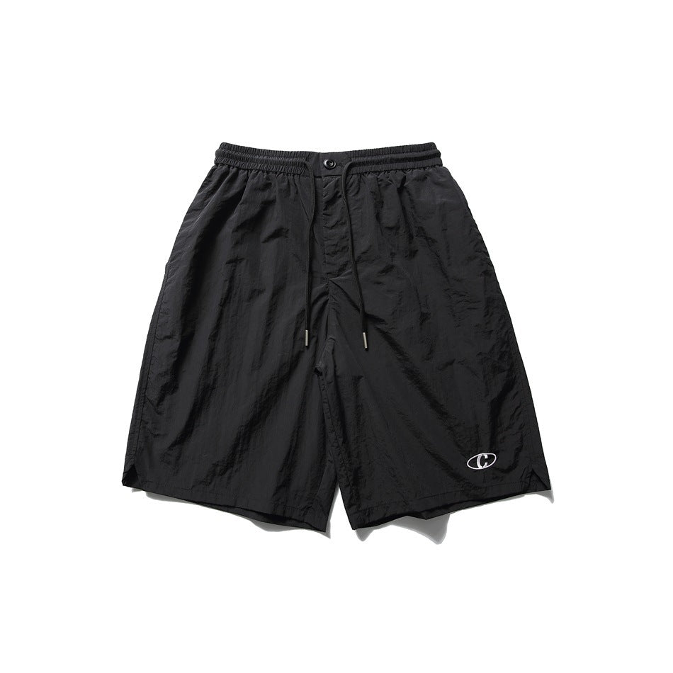 Black knee-length drawstring shorts with elastic waist and small embroidered oval logo, flat front view