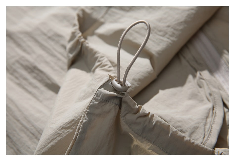 Close-up of a light beige garment with a gathered edge and adjustable elastic drawcord toggle.