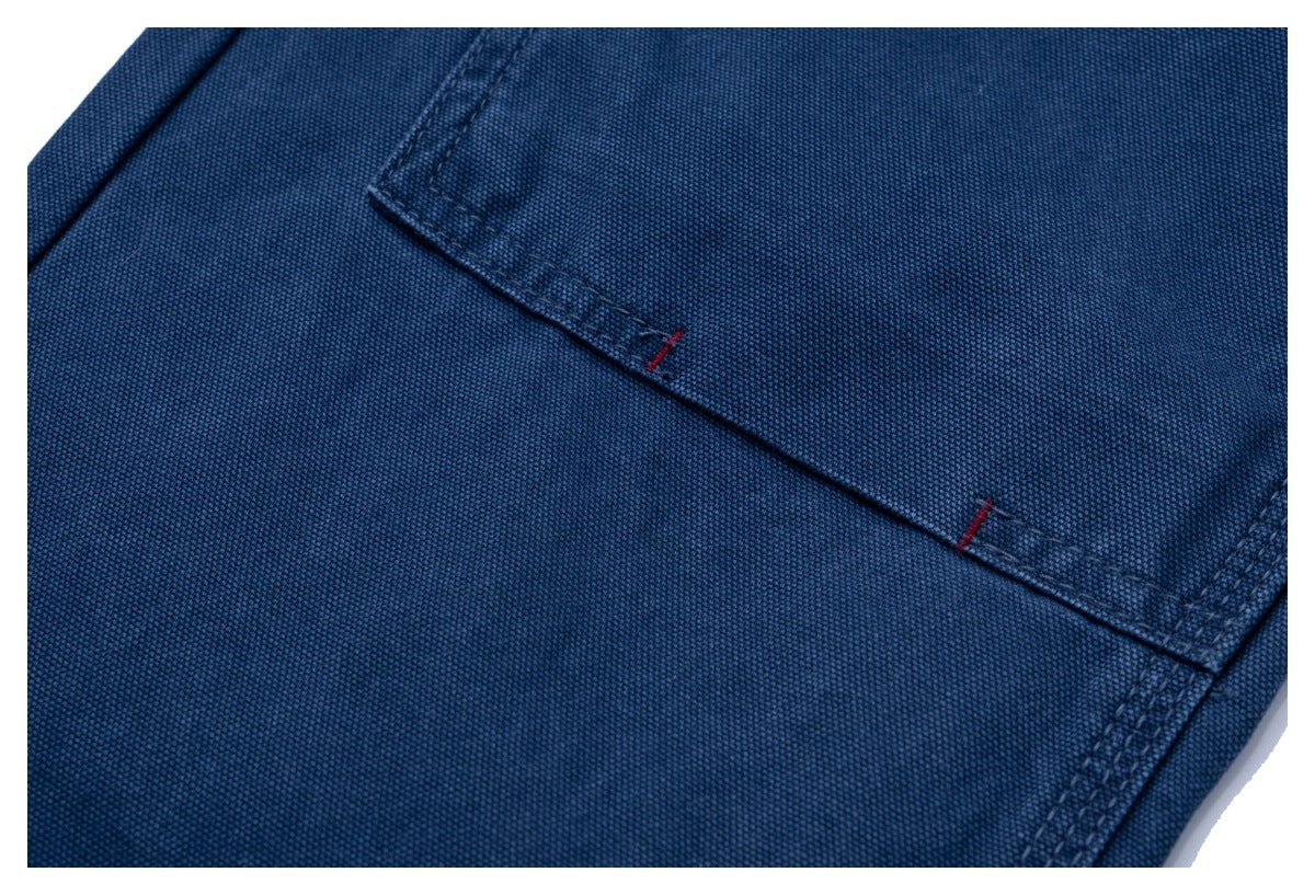 Close-up of a rectangular back pocket with red bar-tack stitching on dark blue trousers.