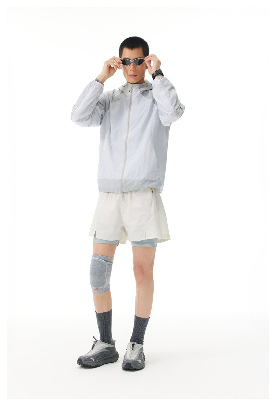 Front view of a model wearing a light gray hooded zip jacket and white shorts over pale blue-gray shorts.