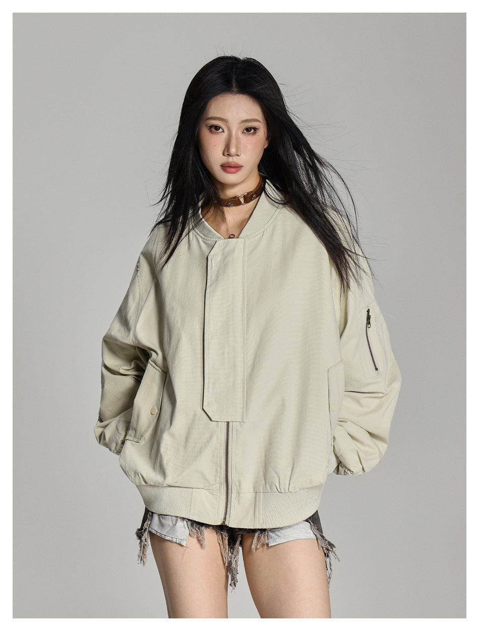 Model wearing a pale beige oversized bomber jacket with a zip sleeve pocket, shown from the front.