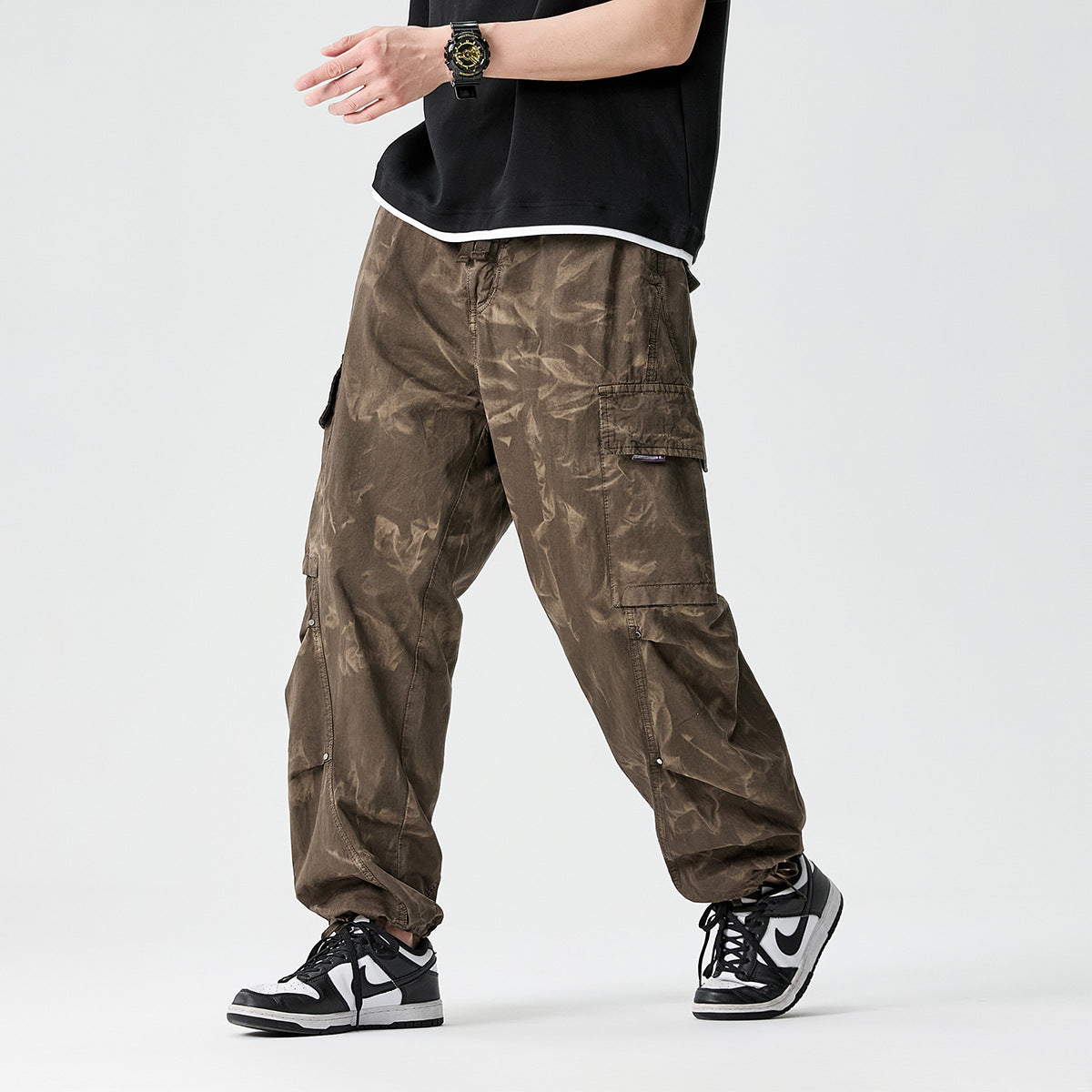 Cropped model wearing loose olive-brown cargo pants with multiple flap pockets and gathered ankles, shown from the front.