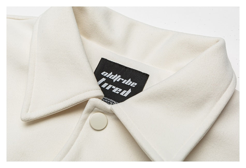 Close-up of an ivory garment's pointed collar, white snap button, and black neck label with white lettering.