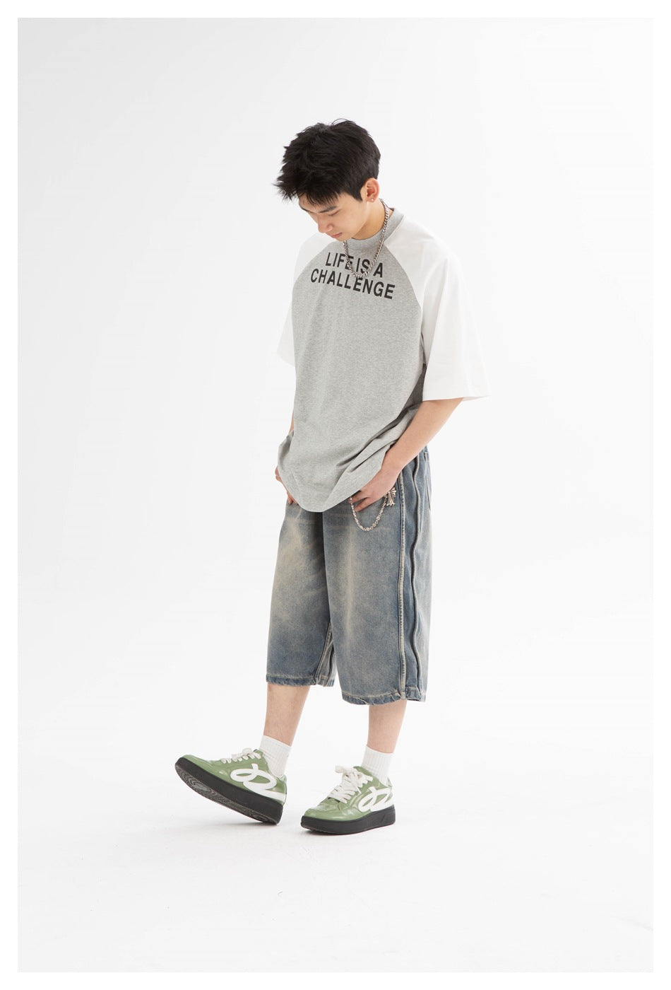 Model in loose faded denim shorts with side seam detail, styled with a chain, gray tee and green sneakers, angled view