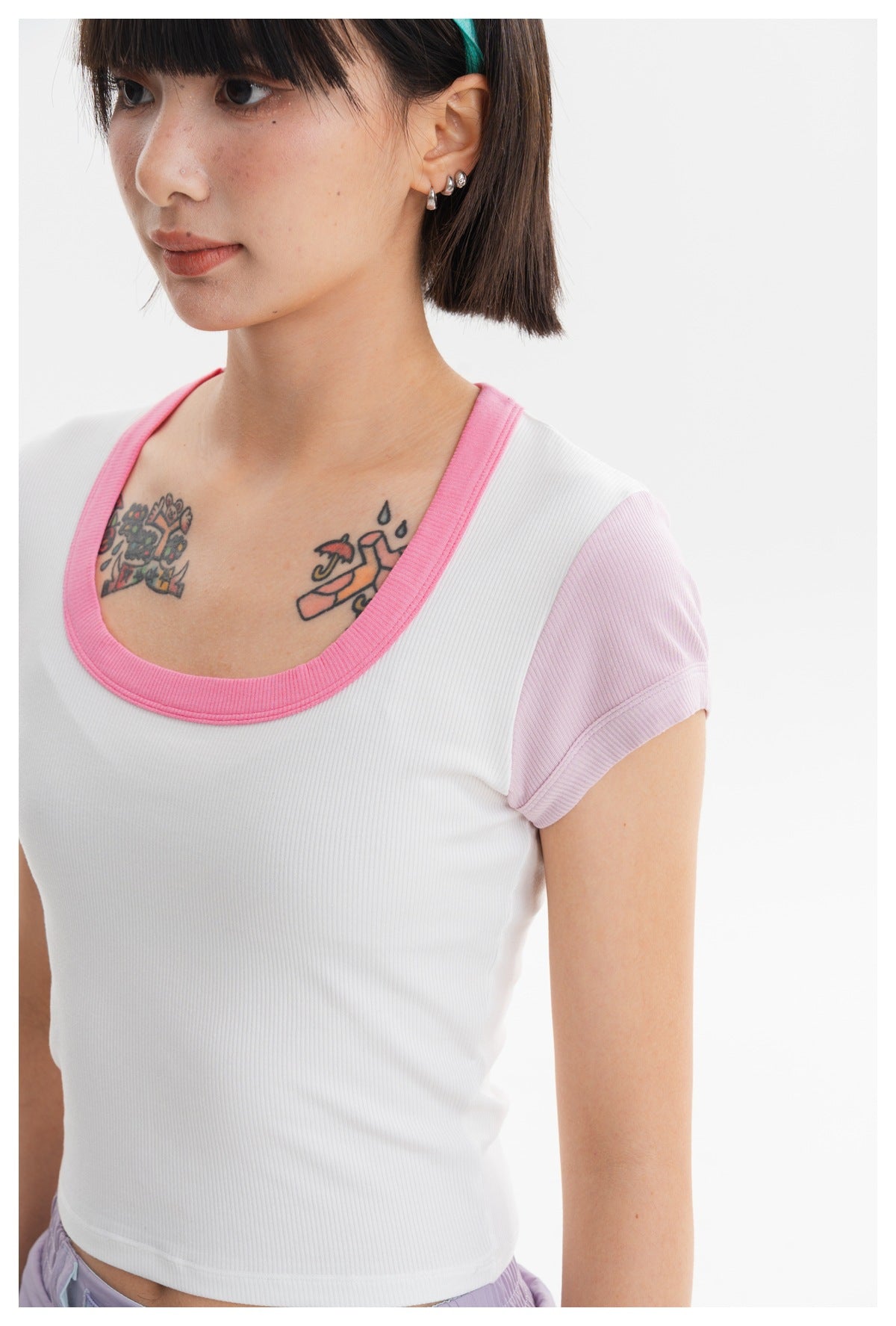 Close-up of a model wearing a white ribbed crop top with a bright pink scoop neckline and pale lilac sleeves.
