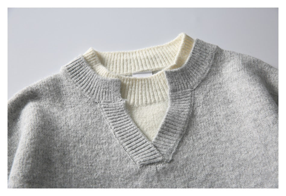 Flat lay of a gray knit V-neck sweater with cream contrast ribbing at the neckline and inner panel.