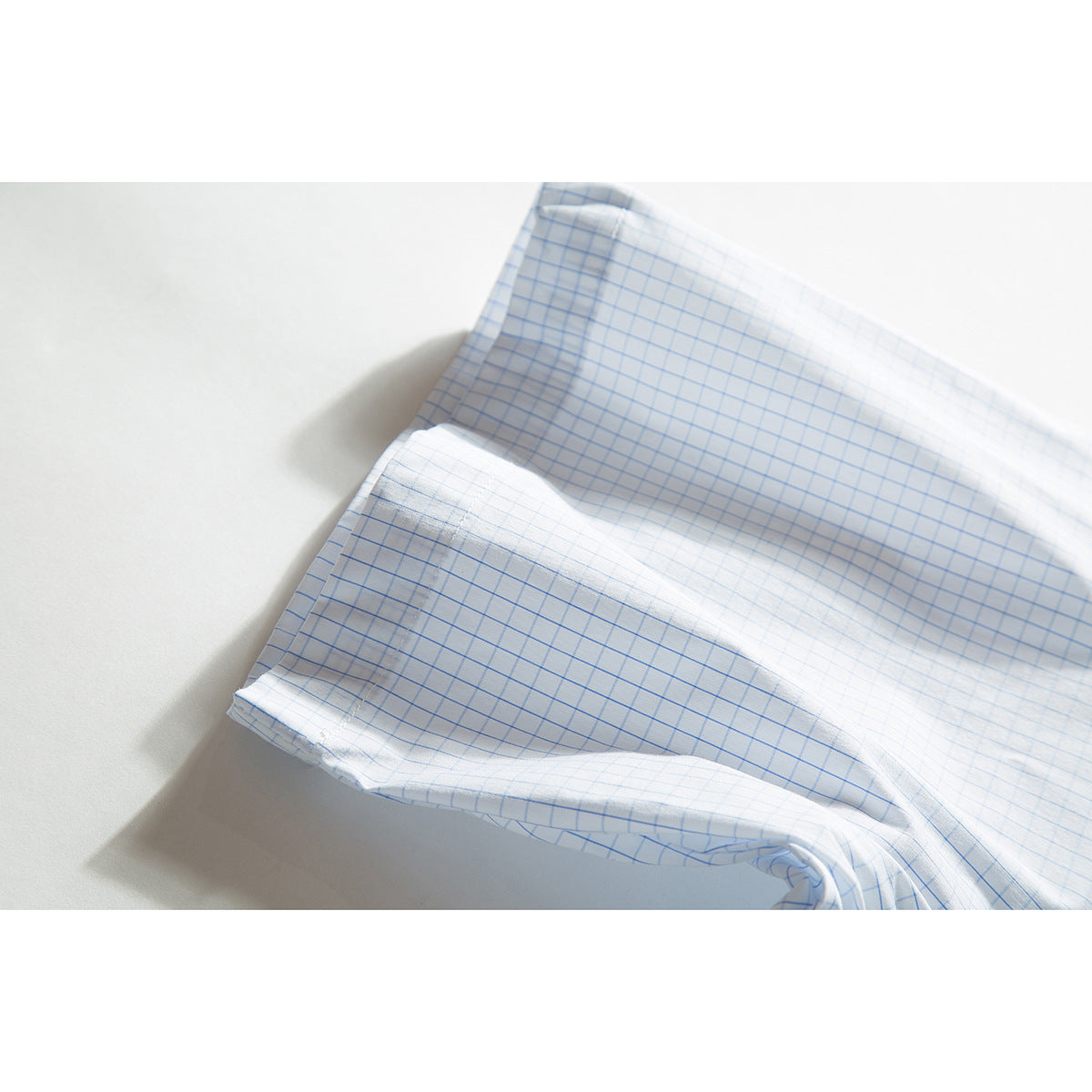 Close-up of the sleeve and cuff of a white shirt with a light blue grid pattern.