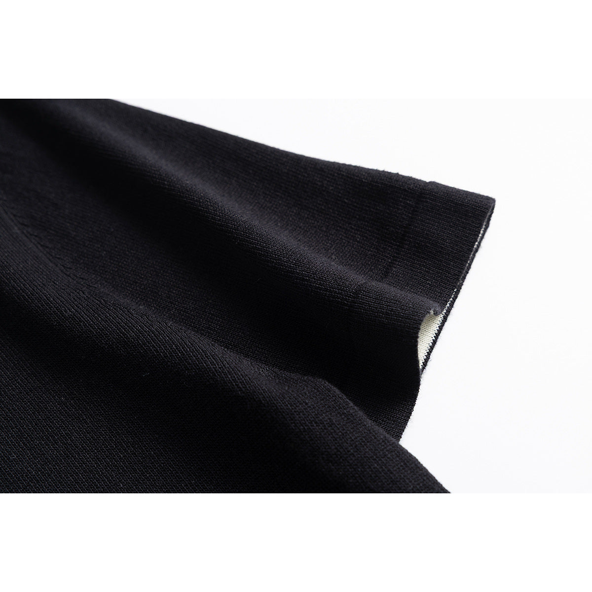 Close-up of a black knit sleeve and cuff, with a small section of cream fabric visible inside.