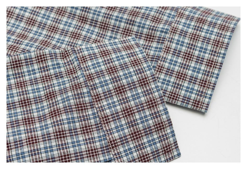 Close-up of a shirt in a blue, burgundy, and white plaid pattern, showing overlapping fabric sections.