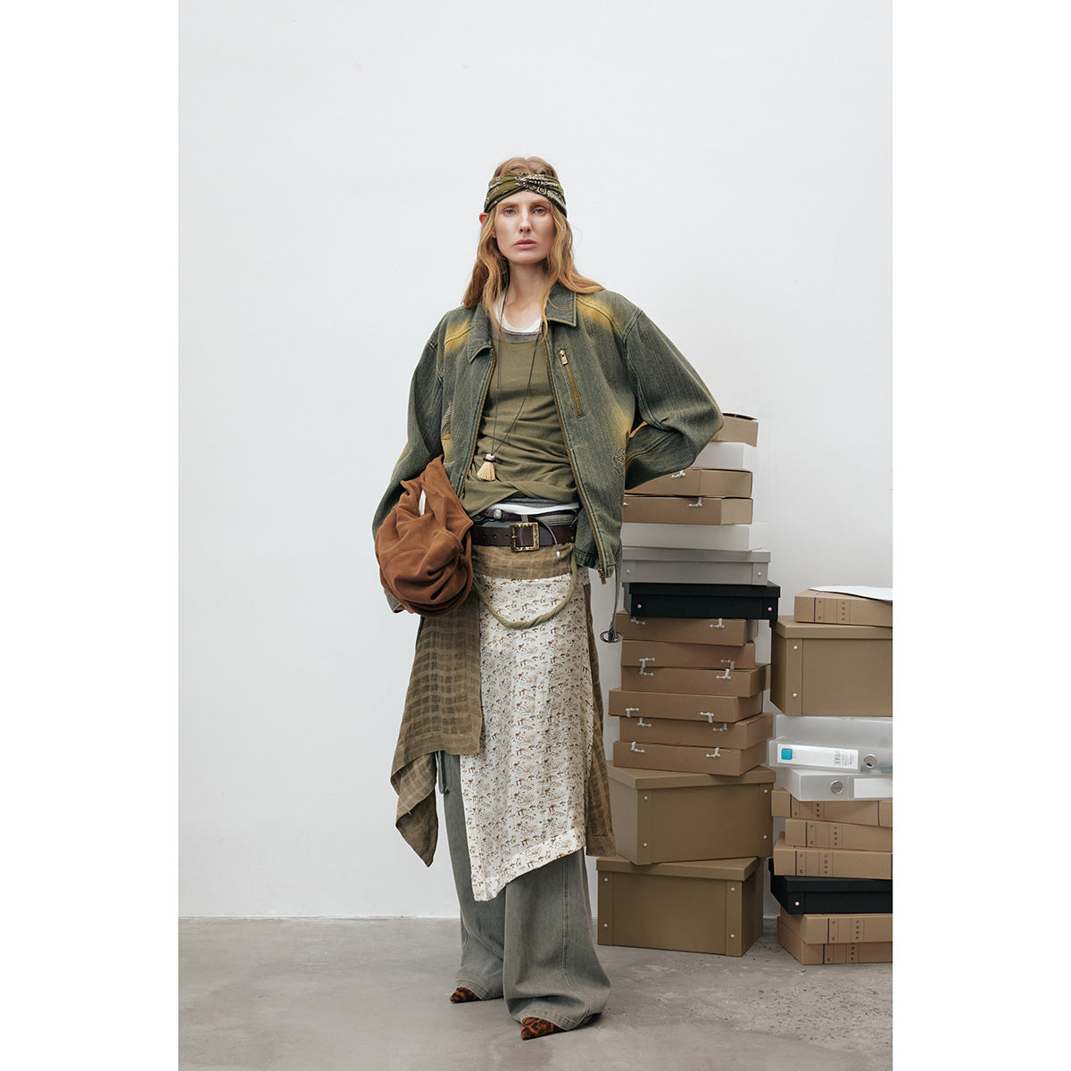 Model wearing an olive distressed zip jacket with embroidered details, layered tops, a patterned skirt and wide-leg trousers.
