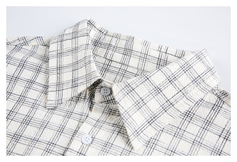 Close-up of the pointed collar and upper button placket on an ivory shirt with a dark plaid pattern.