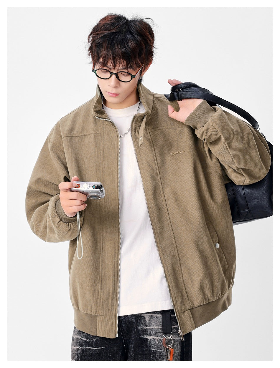 Model wearing open khaki corduroy-look jacket over a white tee, holding a camera and a black bag