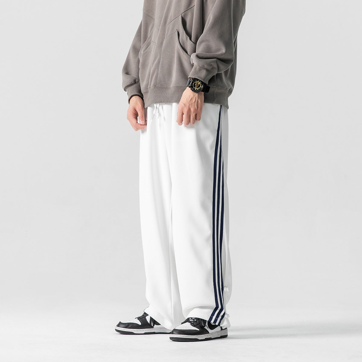 Cropped model wearing loose white track pants with navy side stripes and ankle snaps.