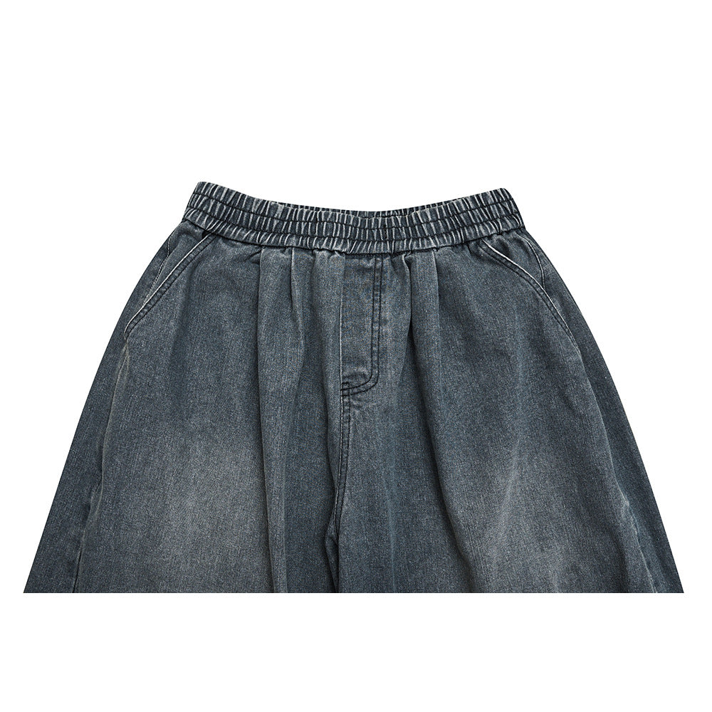 Close-up of the front waist of dark gray denim pants with an elastic waistband and pleated front.