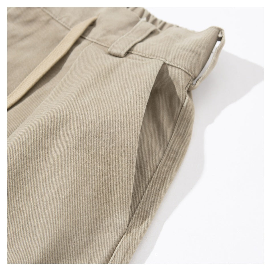 Close-up of beige trousers showing a belt loop, waist tie, and side seam.
