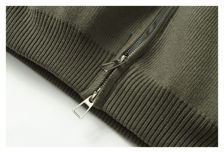 Close-up of two metal zipper pulls near the ribbed hem of an olive-gray knit garment.