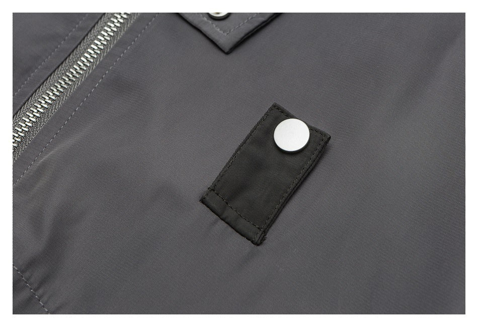 Close-up of a gray jacket chest with a black snap tab and part of the silver zipper.