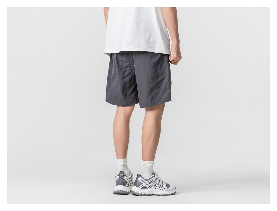 Rear view of a person wearing dark charcoal shorts with a white T-shirt and sneakers.