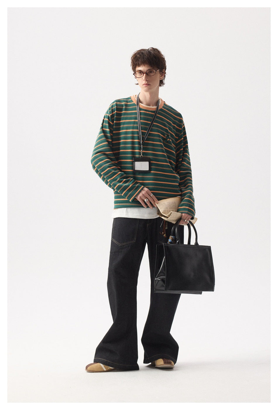 Person wearing a green and orange striped long-sleeve top with dark wide-leg jeans, holding a black tote bag