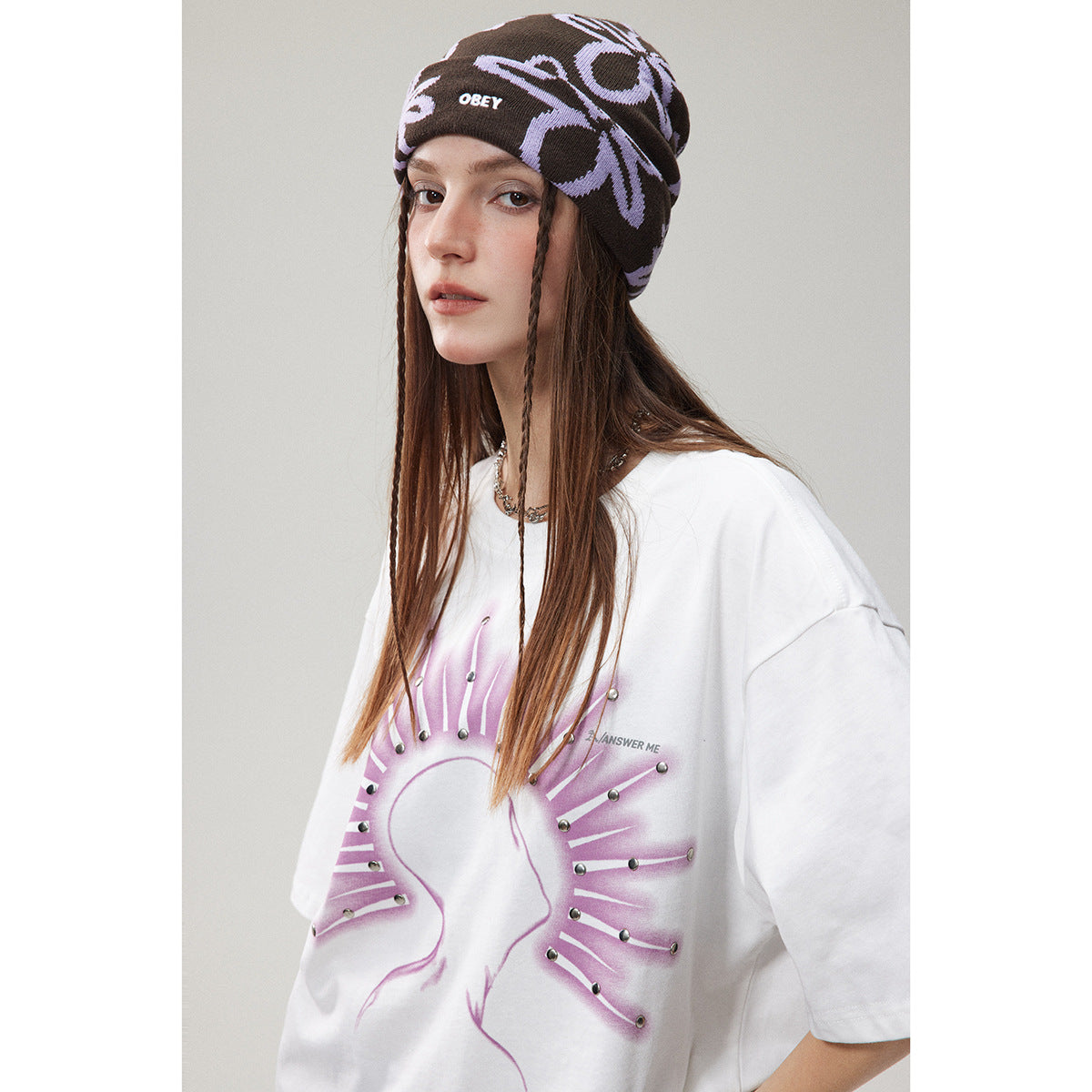 Close portrait of a model in a white oversized T-shirt with a lavender graphic and a dark patterned beanie.