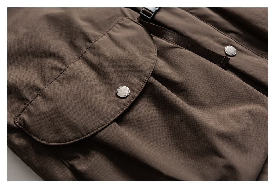 Close-up of a dark brown garment with a rounded flap pocket, silver buttons and an adjustable strap.