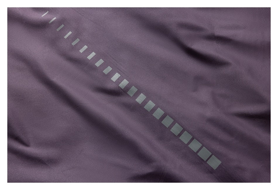 Close-up of a diagonal row of reflective rectangular marks on dark plum fabric.