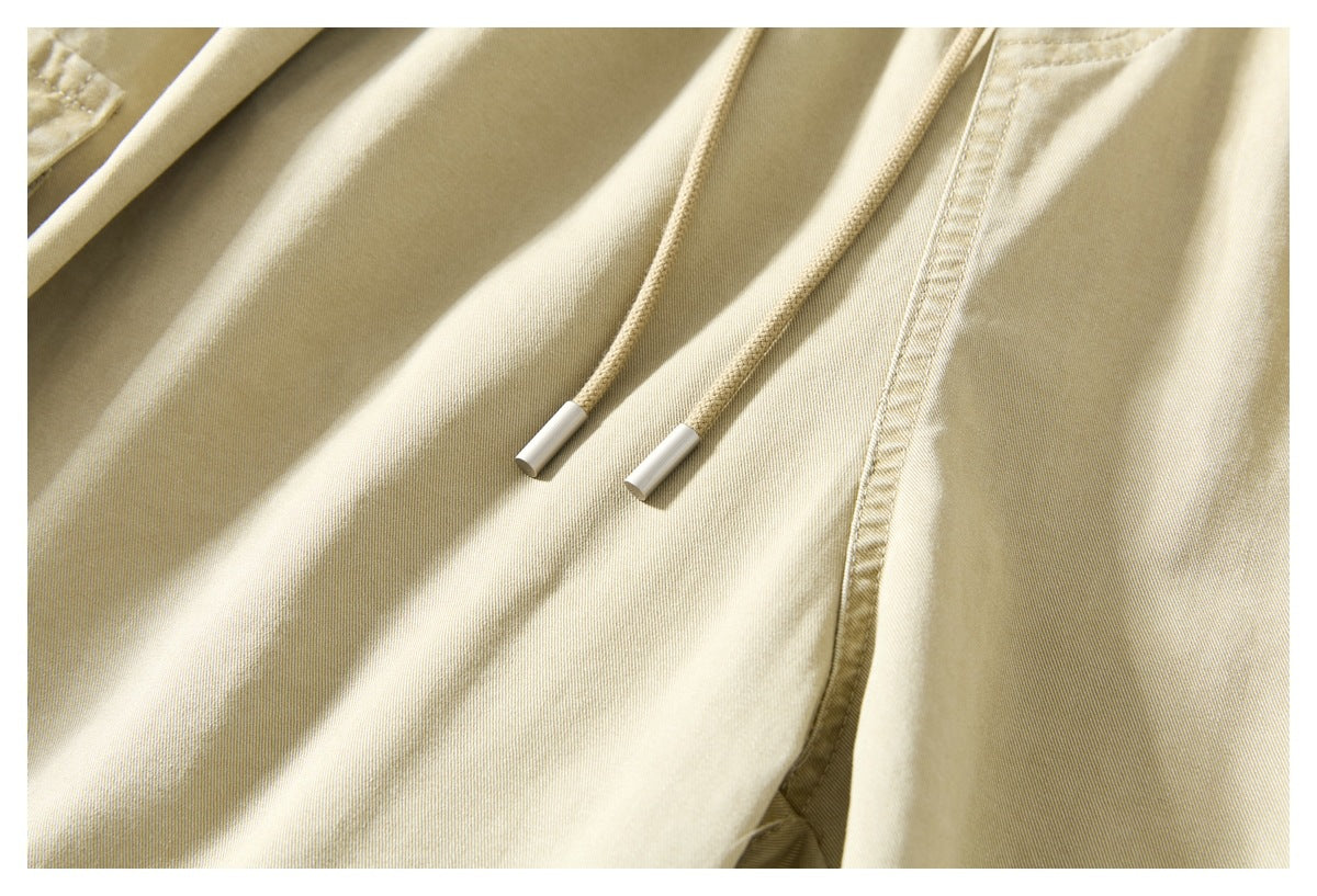 Close-up of beige trousers with two drawstrings and a stitched front seam.