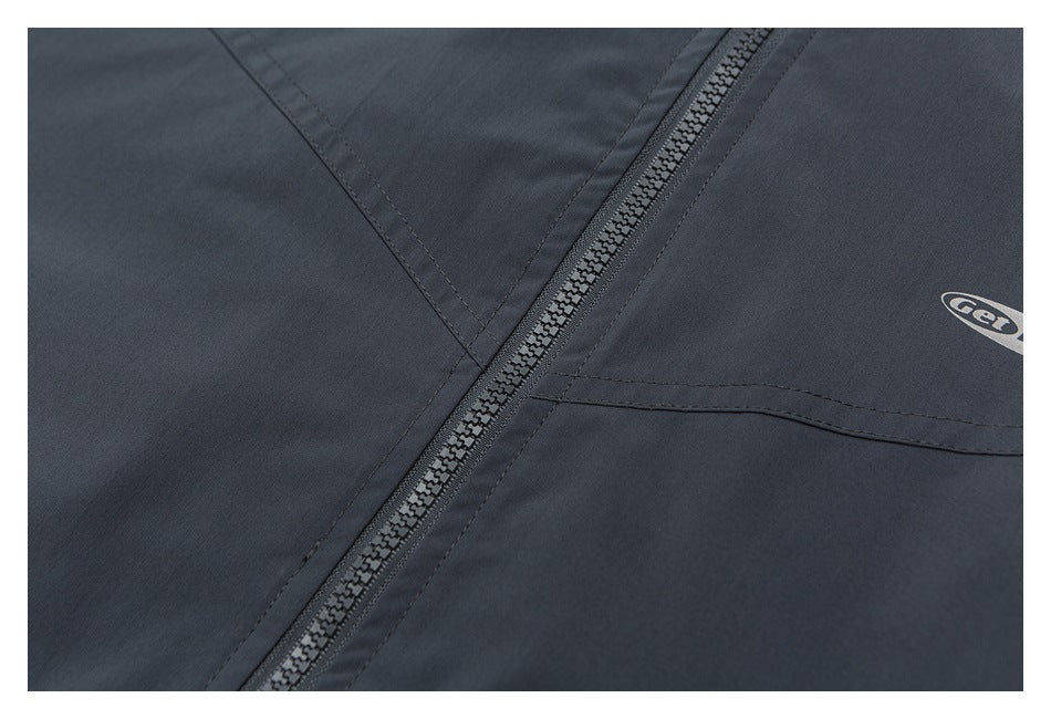 Close-up of a dark charcoal garment showing its zipper, stitched panels, and part of an oval print.