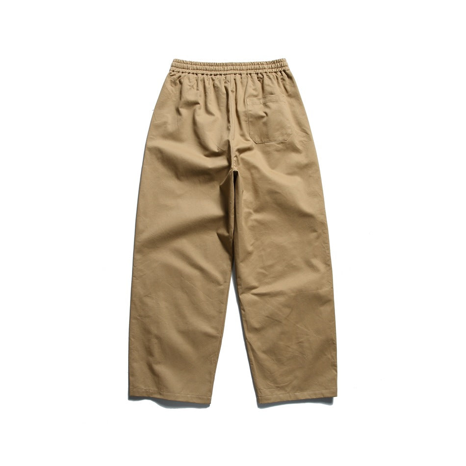Back view of loose-fit tan trousers with an elastic waistband and a single patch pocket.