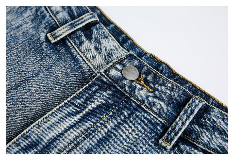 Close-up of the jeans’ metal waist button, belt loop and contrast stitching on faded blue denim.