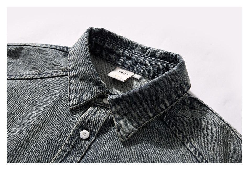 Inset close-up of a dark gray washed denim shirt collar, neckline, and white button.