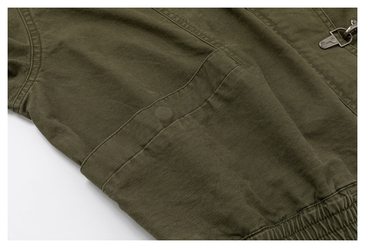 Close-up of an olive drab garment with stitched panels, a metal zipper pull, and a gathered edge.