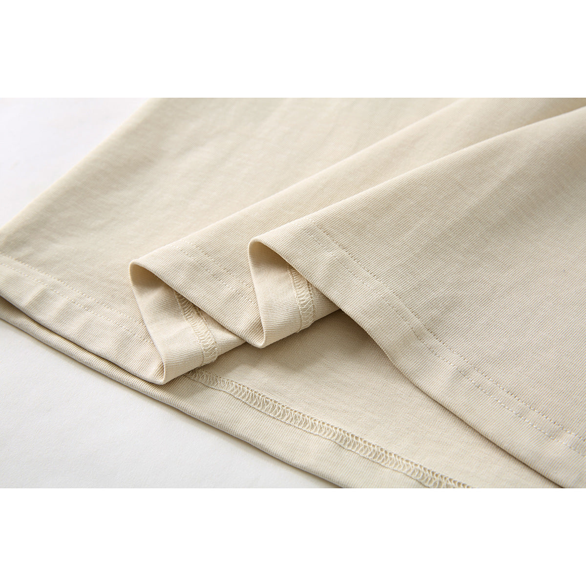 Close-up of the cream T-shirt's folded hem, showing the stitching and inside seam finish.