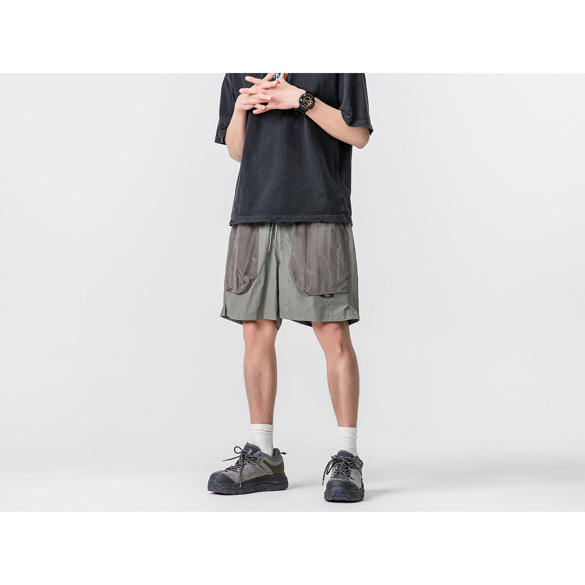 Cropped model wearing olive-gray shorts with oversized dark front pockets, a drawstring waist and a black T-shirt.