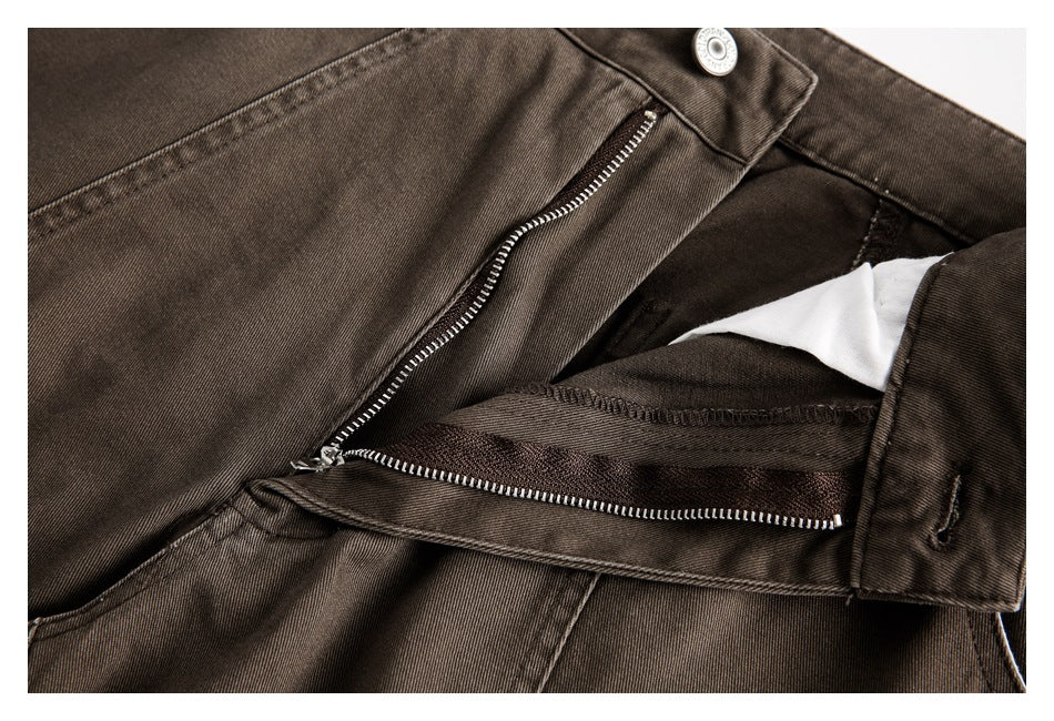 Close-up of brown trousers showing the open metal zipper fly, button, and inner waistband.