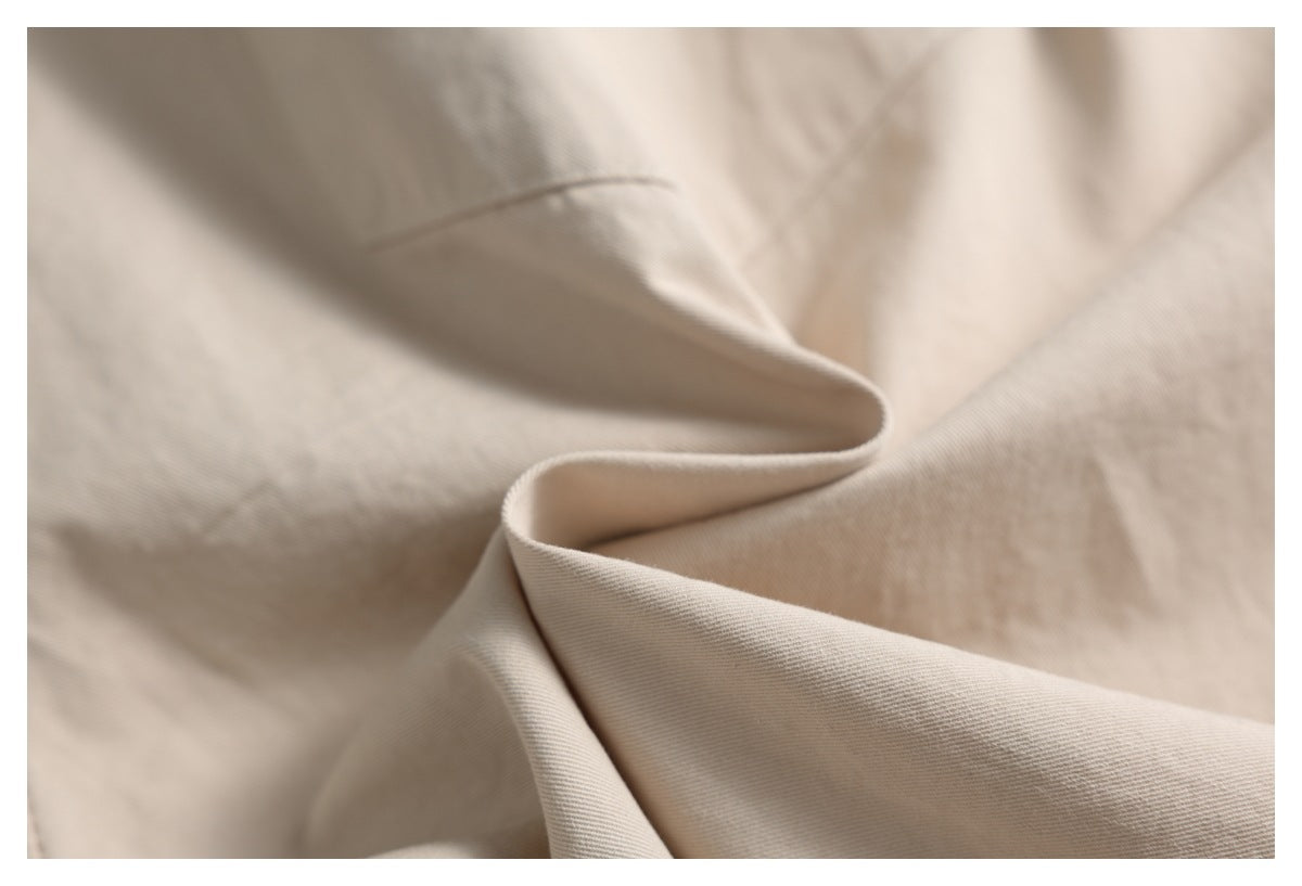 Close-up of light beige fabric folded into soft draped curves, showing a fine diagonal weave.