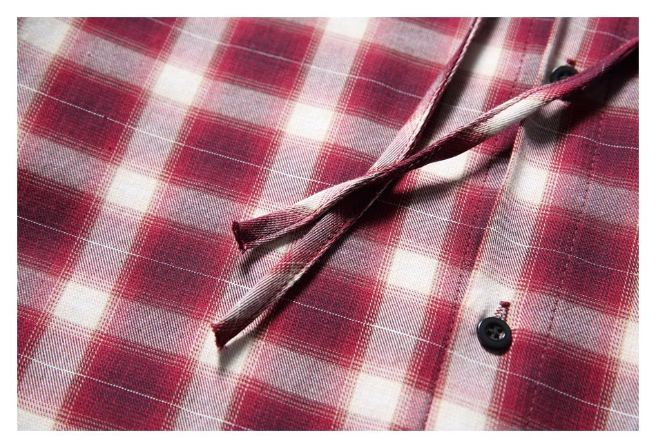 Close-up of the red and cream plaid shirt's front placket, black button, and narrow fabric ties.