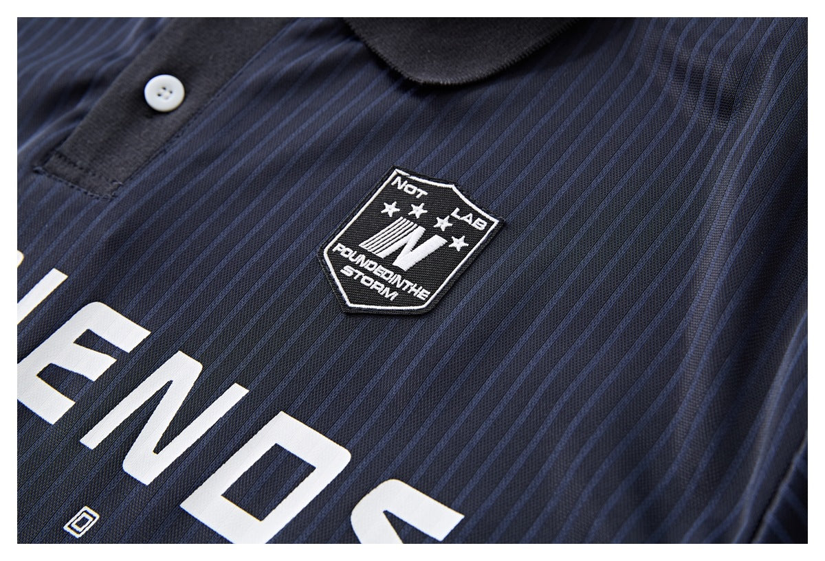 Close-up of a dark navy pinstriped polo shirt with a black collar, white button, embroidered shield patch and partial white
