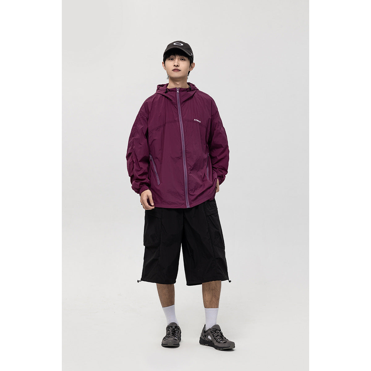 Full-length front view of a model wearing a plum hooded zip jacket with black shorts.