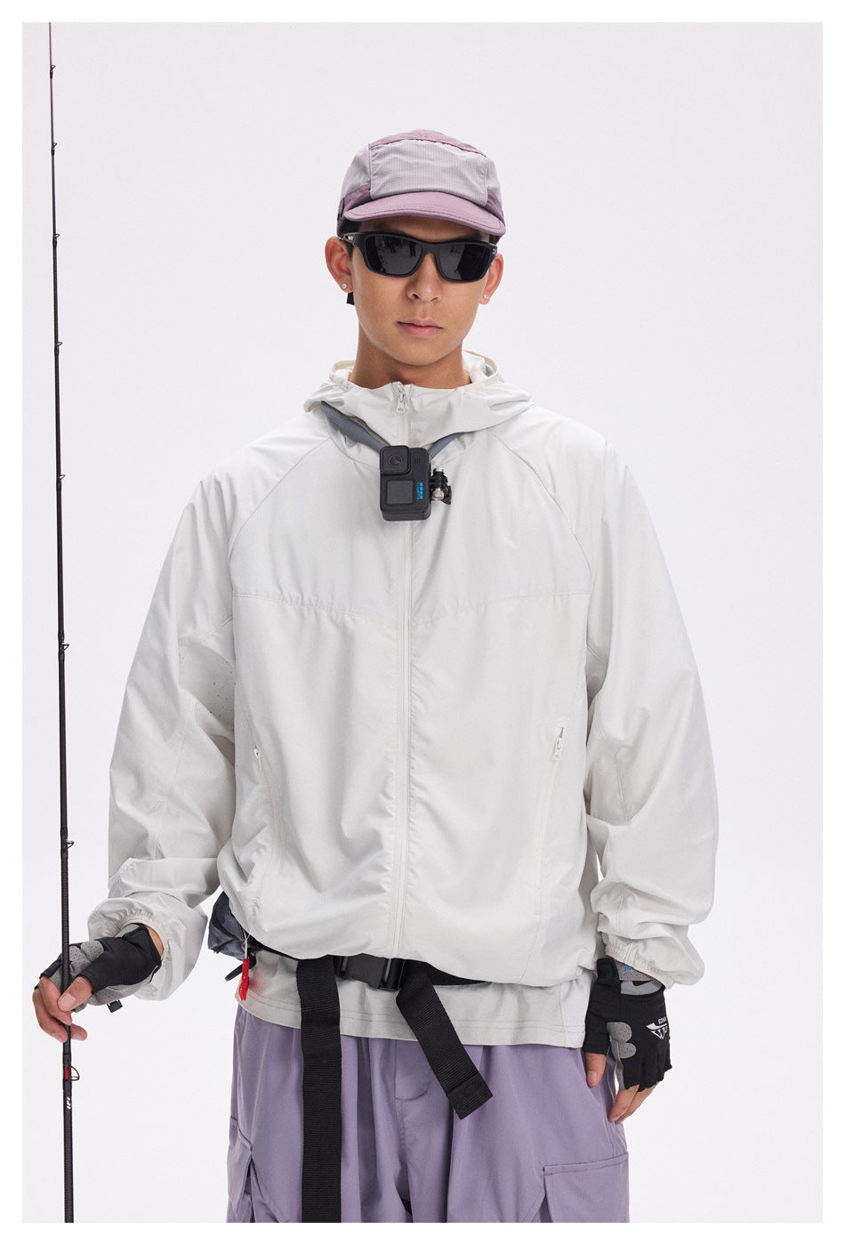 Front view of a model wearing a white hooded zip jacket and lavender cargo pants with a mauve cap and sunglasses.