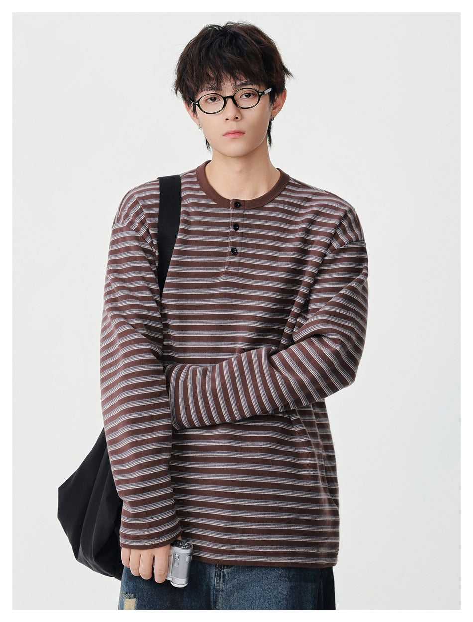 Model wearing a brown striped long-sleeve henley-style top with black buttons, with a black bag over the shoulder