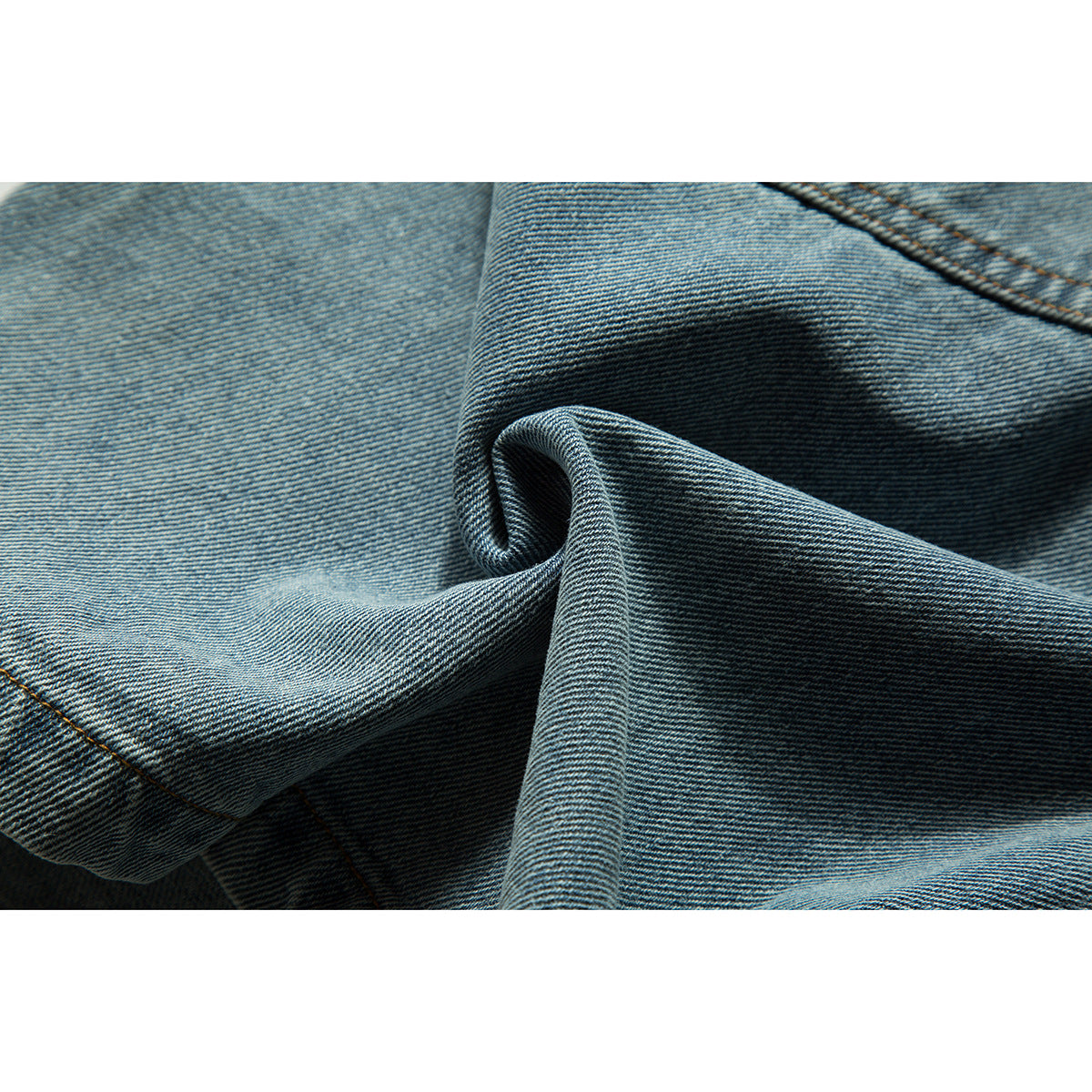 Extreme close-up of blue denim fabric folded to show its diagonal weave and stitching.