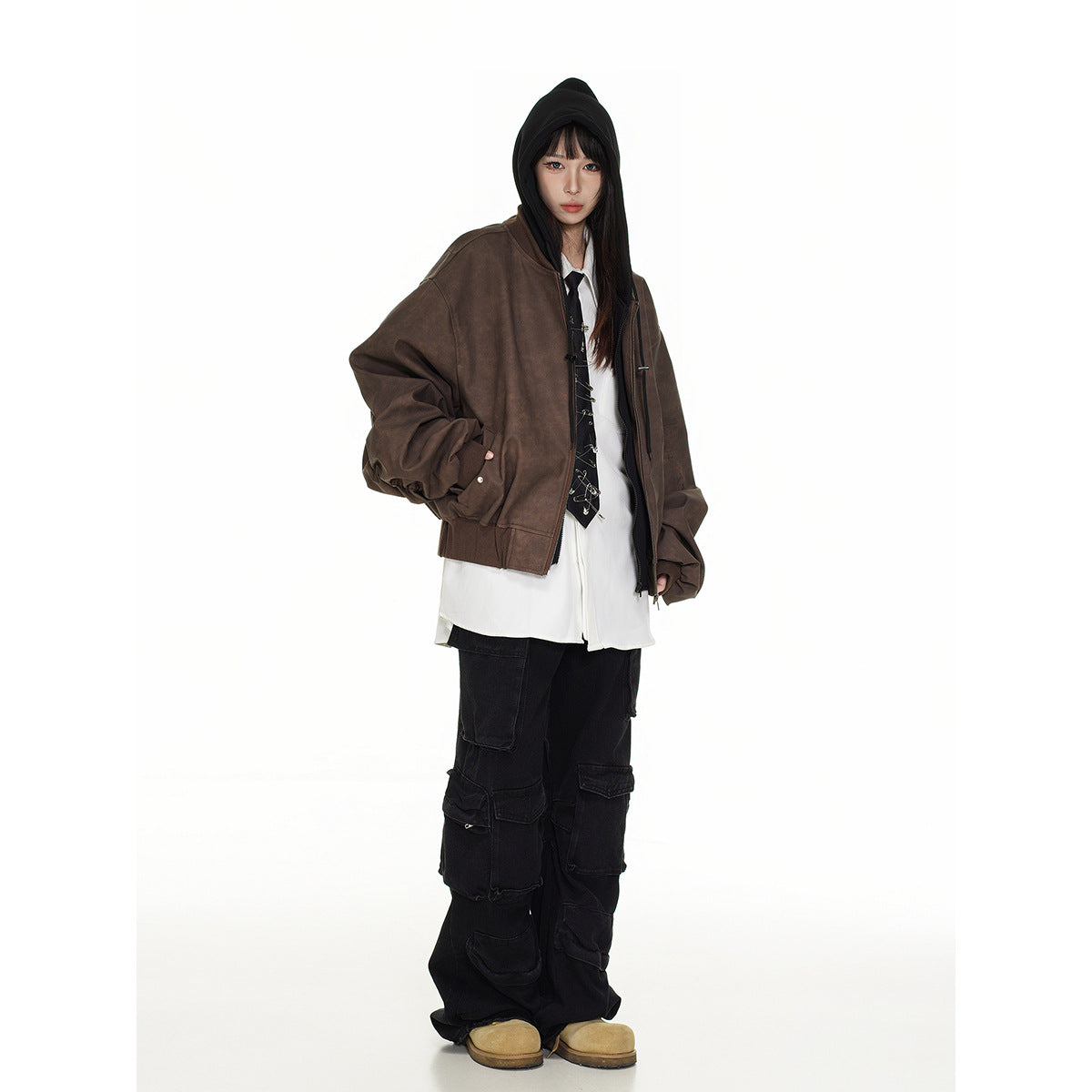 Model wearing an oversized brown jacket over a black hood, white shirt and tie, with loose black cargo pants.