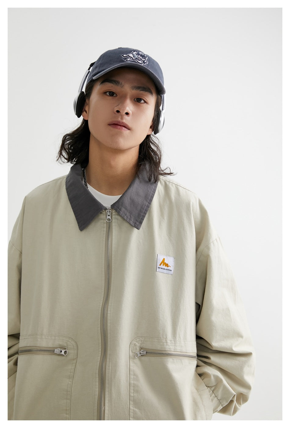 Close front view of a model wearing a light khaki jacket with a gray pointed collar and zippered pockets.
