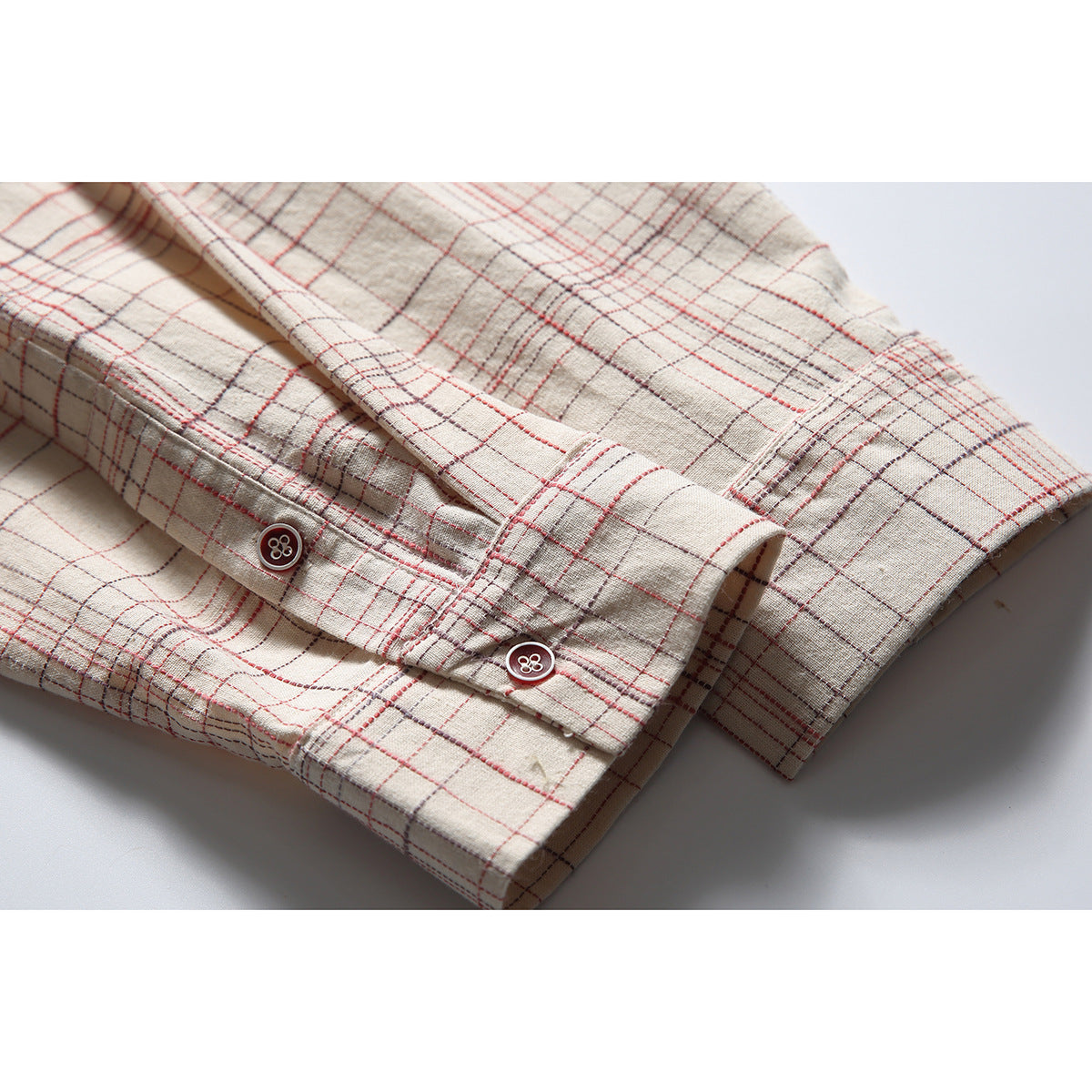 Close-up of the off-white plaid shirt's buttoned sleeve cuff, with red and gray grid lines.